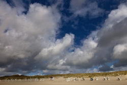 Dramatischer Himmel über Dünenlandschaft mit Strandkörben und einer kleinen Hütte.