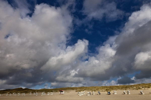 Dramatischer Himmel über Dünenlandschaft mit Strandkörben und einer kleinen Hütte.