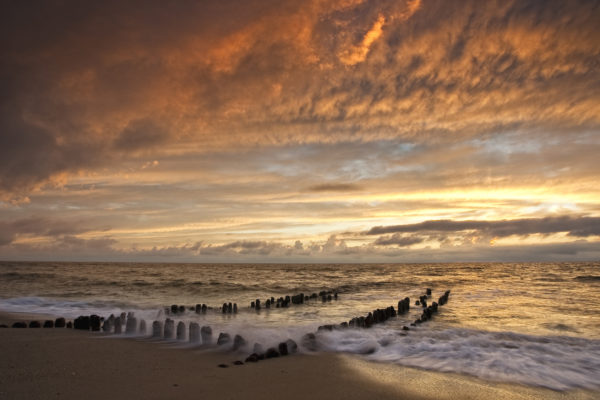 Beeindruckender Sonnenuntergang über einem rauen Meer mit alten Holzpfählen am Strand von Sylt.