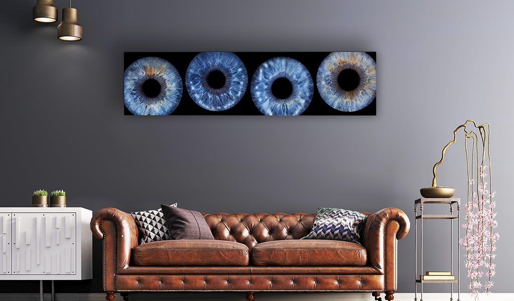 Vier-teiliges Iris-Wandbild mit blauen Augen in verschiedenen Nuancen, präsentiert über einem braunen Ledersofa in einem modernen Raum mit grauen Wänden.