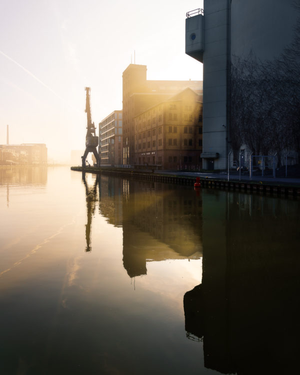 Silhouette des historischen Hafenkrans im Stadthafen Münster, eingefangen im Gegenlicht der Sonne von Sascha Talke, spiegelt sich im ruhigen Wasser.