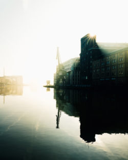 Münsteraner Hafenkran und Wolfgang Borchert Theater im eindrucksvollen Gegenlicht, mit Spiegelungen im ruhigen Hafenwasser.