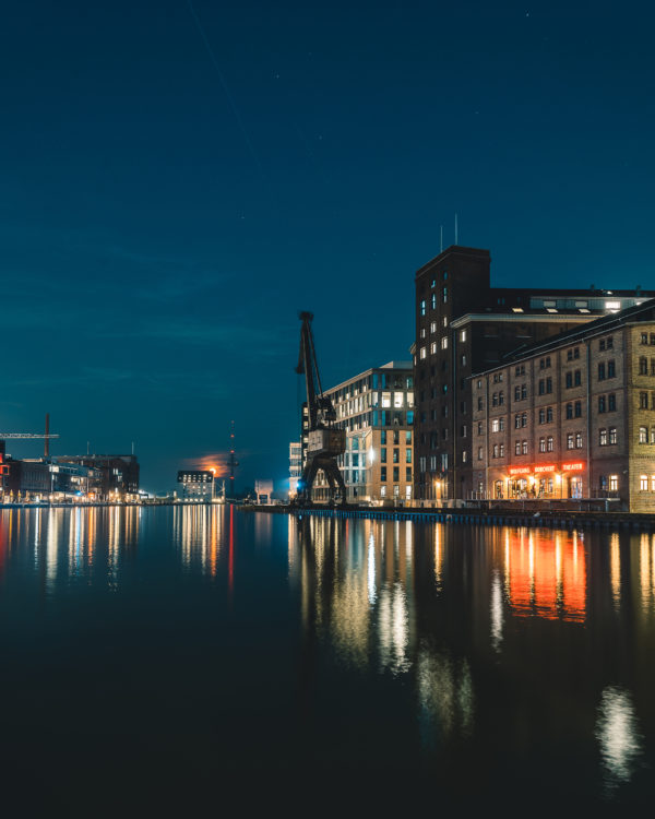 Klare Wasserspiegelung im Stadthafen von Münster bei Nacht, mit Blick auf beleuchtete Gebäude und den Hafen-Kran, fotografiert von Sascha Talke.