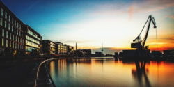 Morgendliche Stimmung am Stadthafen Münster mit dem Hafen-Kran und modernen Gebäuden, die sich im ruhigen Wasser spiegeln.
