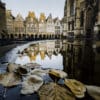 Herbstliche Blätter treiben auf dem Wasser des Lambertus-Brunnens mit der Spiegelung des Prinzipalmarkts und der St. Lamberti Kirche im Hintergrund in der Altstadt von Münster.