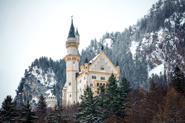 Schloss Neuschwanstein im Winter, umgeben von schneebedeckten Bäumen und Bergen.