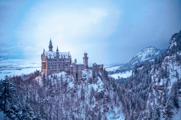 Schloss Neuschwanstein in einer winterlichen Landschaft, umgeben von verschneiten Wäldern und Bergen.