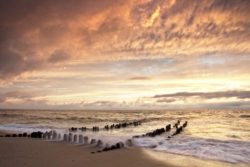 Beeindruckender Abendhimmel über rauer See mit alten Holzpfosten im Vordergrund am Strand.