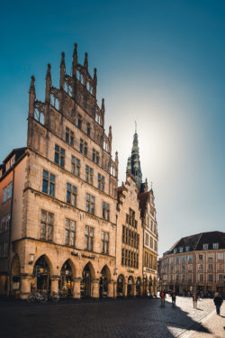 Sonnendurchflutetes Historisches Rathaus von Münster am Prinzipalmarkt, belebt durch Passanten.