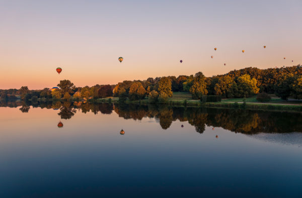 Aasee in Münster bei Sonnenuntergang, spiegelnde Wasseroberfläche, farbenfroher Himmel, Montgolfiade-Ballons im Hintergrund Beschriftung: Münster Aasee Sonnenuntergang - Montgolfiad