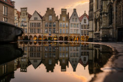 Die Fassaden des Prinzipalmarkts in Münster spiegeln sich im Wasser des Lambertus-Brunnens während der Abenddämmerung, fotografiert von Sascha Talke.