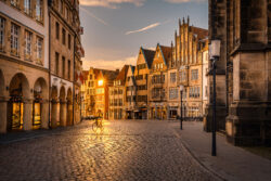 Radfahrer fährt im Gegenlicht über den Prinzipalmarkt in Münster, umgeben von historischen Giebelhäusern während der goldenen Stunde.