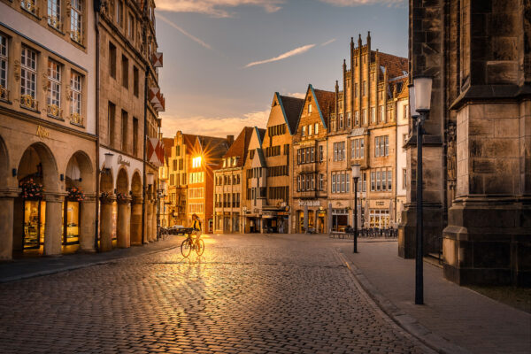 Radfahrer fährt im Gegenlicht über den Prinzipalmarkt in Münster, umgeben von historischen Giebelhäusern während der goldenen Stunde.