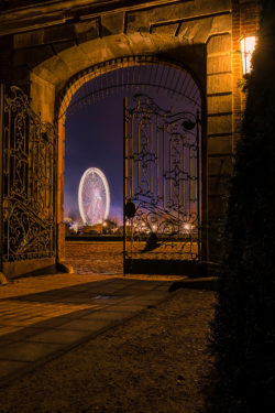 Blick durch ein historisches Tor auf das erleuchtete Riesenrad des Send Volksfestes bei Nacht in Münster.