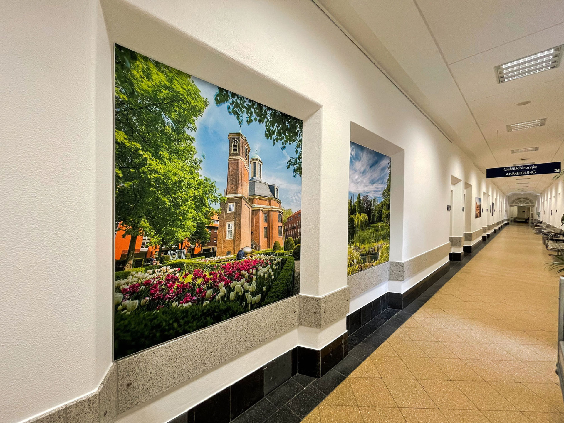 Ein langer Flur im Franziskushospital mit Bildern von feine art mit Münster-Motiven an den Wänden