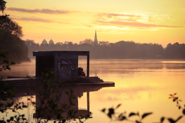 Junge Leute auf Jorge Pardo Pier am Aasee, Münster, Morgensonne und Silhouette von Lambertikirche und Domtürmen