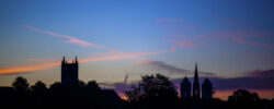 Silhouette von Münsters Altstadt mit St. Lamberti, St.-Paulus-Dom und Liebfrauen-Überwasserkirche vor einem malerischen Himmel in Blau und Orange, durchzogen von wenigen langgezogenen Wolken, eingefangen von Jonas Hofmann im Stoffdruck "MS4life".