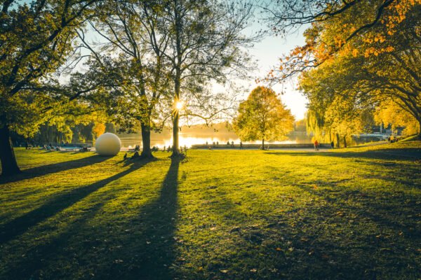 Menschen genießen Sonne auf Wiese vor Aasee mit Aaseekugel im Hintergrund