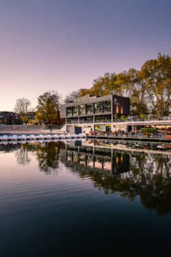 Aaseeterassen in Münster mit lila-rotem Himmel, ruhigem Aasee und Tretbooten am Pier.