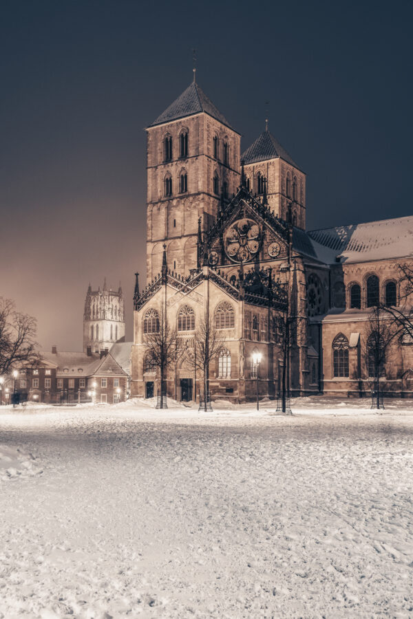 Winterliche Ansicht des Domplatzes in Münster mit dem St.-Paulus-Dom im Hintergrund, umgeben von unberührtem Schnee.