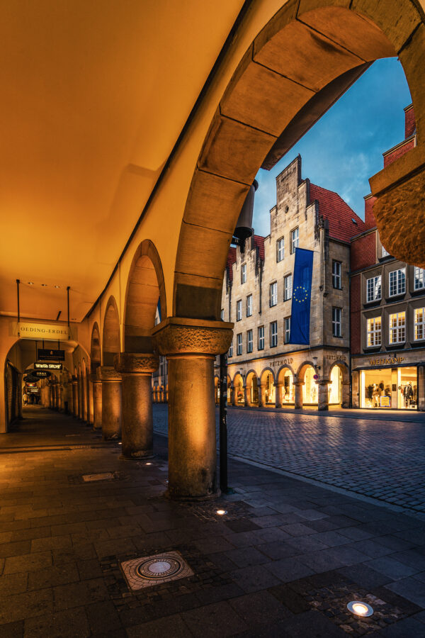 Stimmungsvolle Nachtansicht des Prinzipalmarkts in Münster mit beleuchteten Arkaden und historischen Gebäuden.