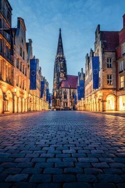 Hochformat Foto des Prinzipalmarkts in Münster, mit historischen Gebäuden, Europafahnen und der Lambertikirche im Hintergrund.