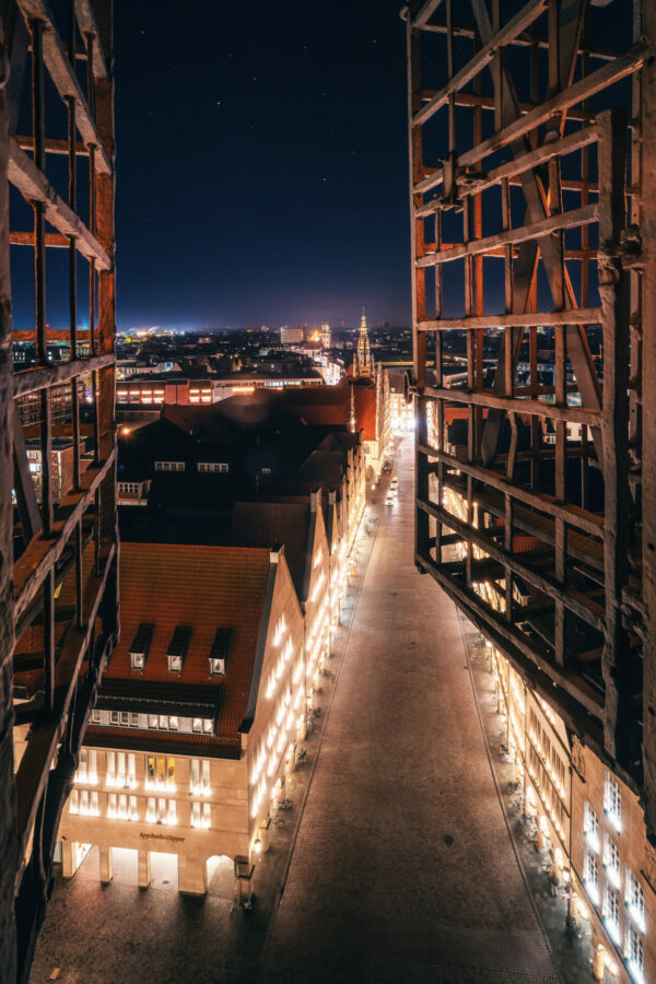 Eine nächtliche Aufnahme von Münster, mit dem erleuchteten Prinzipalmarkt und St. Lamberti, umrahmt von einem strahlenden Sternenhimmel.