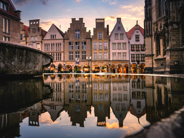 Ansicht des Lambertibrunnens mit reflektierenden Gebäuden im Wasser auf dem Lambertikirchplatz in Münster.